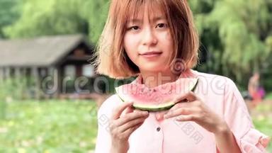 夏天的女人吃西瓜片。 微笑着在公园里吃西瓜的中国女孩。 假日生活方式。 夏季概念。